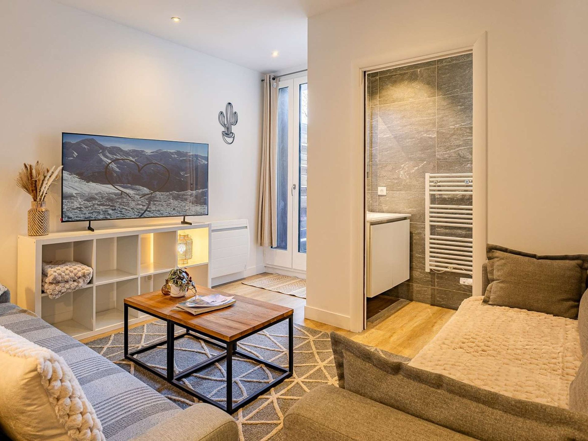 Un salon moderne avec un téléviseur, un canapé, une table basse et une vue sur l’extérieur.