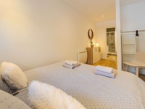 Una camera da letto con un letto, un comodino in legno, uno specchio, una sedia bianca e un bagno sullo sfondo.