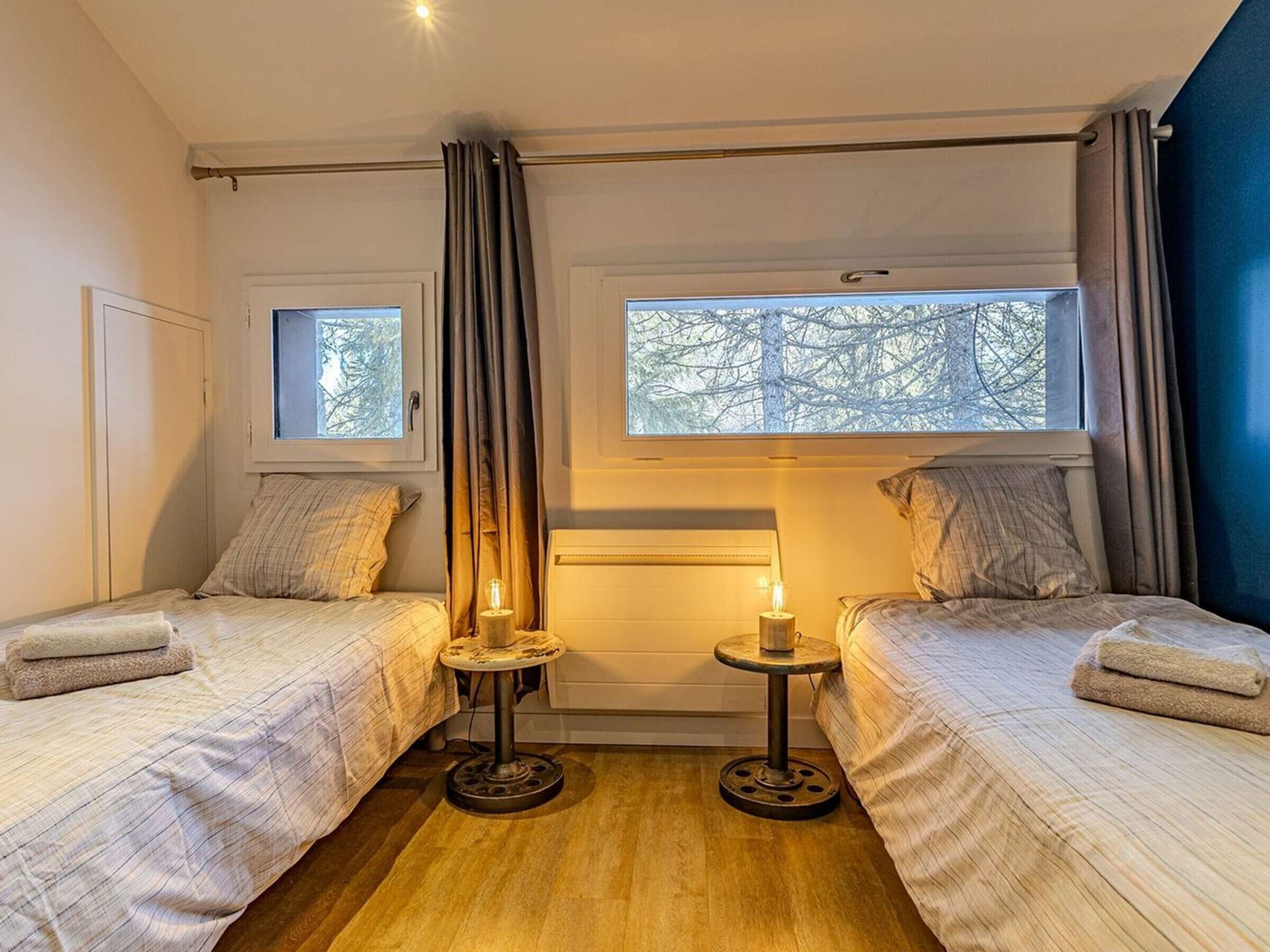 Ein Schlafzimmer mit zwei Betten, einem Fenster, einem Nachttisch mit Lampe und einem Vorhang.