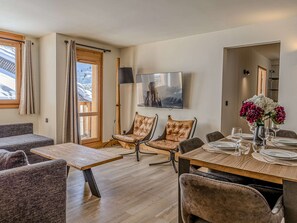 Ein Essbereich mit einem Holztisch, gedeckt für vier Personen, zwei gepolsterten Stühlen, einer Couch und einem an der Wand befestigten Fernseher.