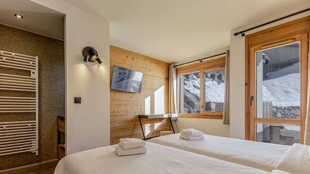 Hotellihuone, jossa on kaksi sänkyä, seinälle asennettu televisio, puusäleistä tehty seinä ja ikkuna, josta avautuu näkymä lumiseen maisemaan.