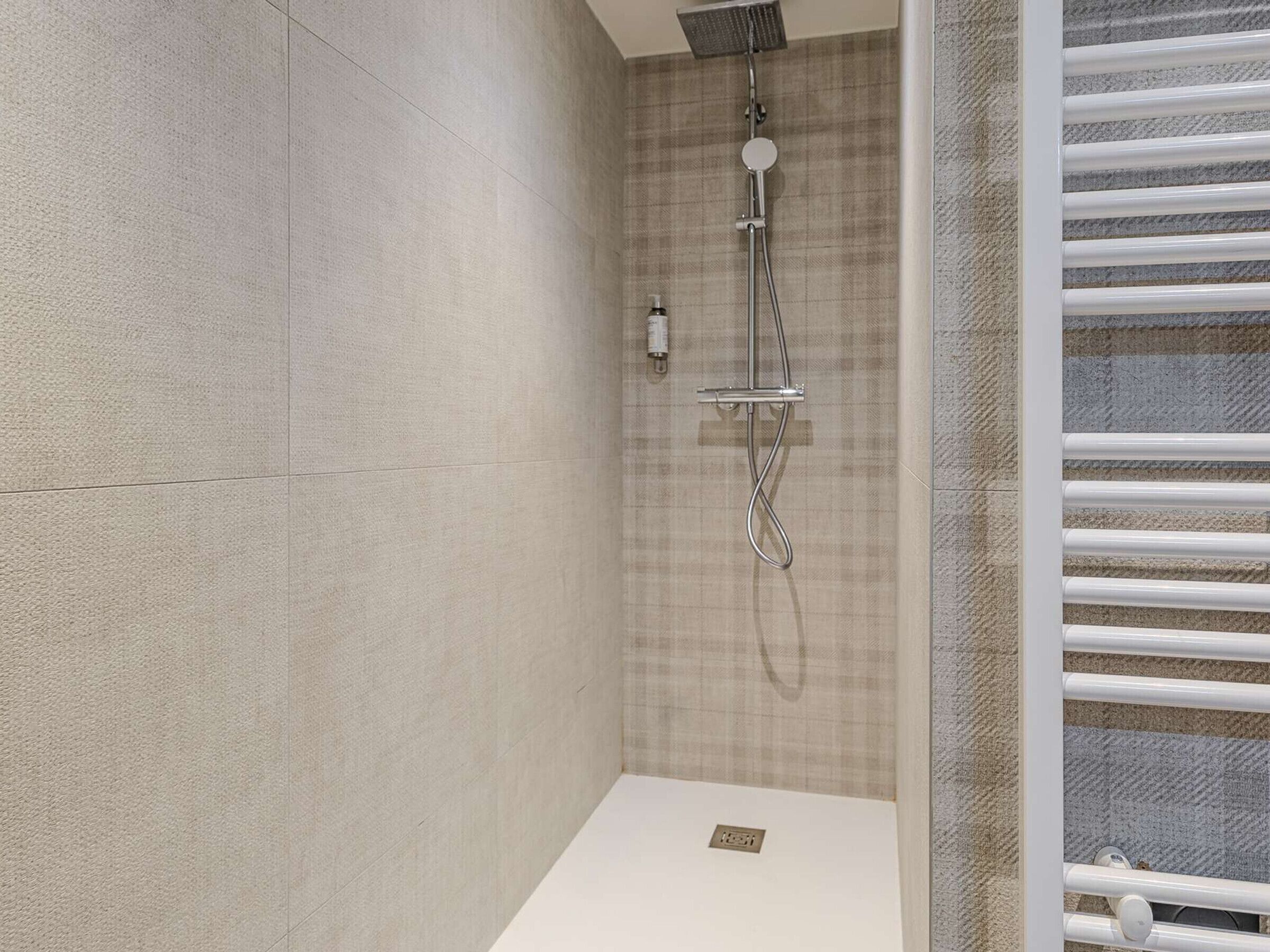 A modern shower with a handheld showerhead and a wall-mounted control panel.