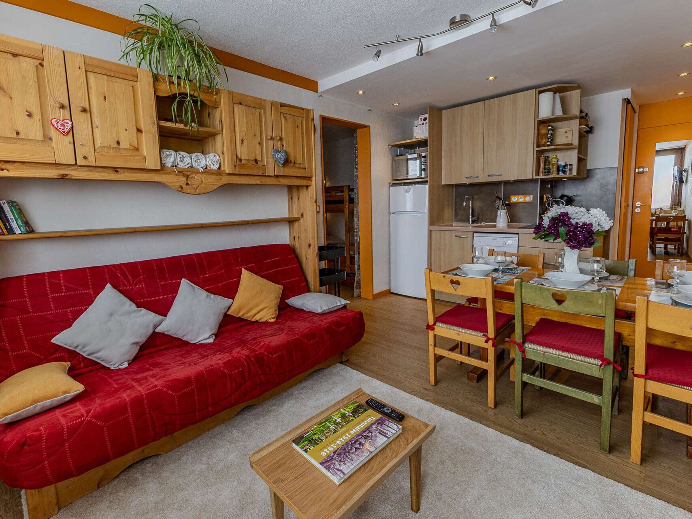Un espacio habitable pequeño con un sofá rojo, armarios de madera, una mesa de comedor con sillas y una zona de cocina.