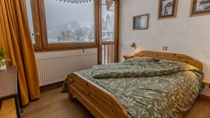 Et soveværelse med en træseng, et vindue med udsigt til sneklædte træer, og en radiator.