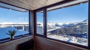 Eine Holzhütte mit großen Fenstern und Blick auf schneebedeckte Berge und einen See.
