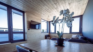 Ein modernes Interieur mit Holzbalkendecke, großen Fenstern, einem Esstisch und einem Blumentopf.