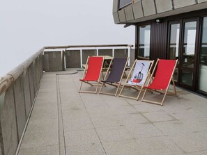 Una terrazza sul tetto con quattro poltrone relax, una ringhiera e un edificio con ampie finestre.