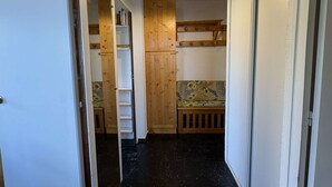 Een smalle gang met een houten bankje, een zithoekje en een boekenkast.