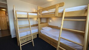Een slaapkamer met twee houten stapelbedden, elk met een trapje, en een klein bureau in de hoek.