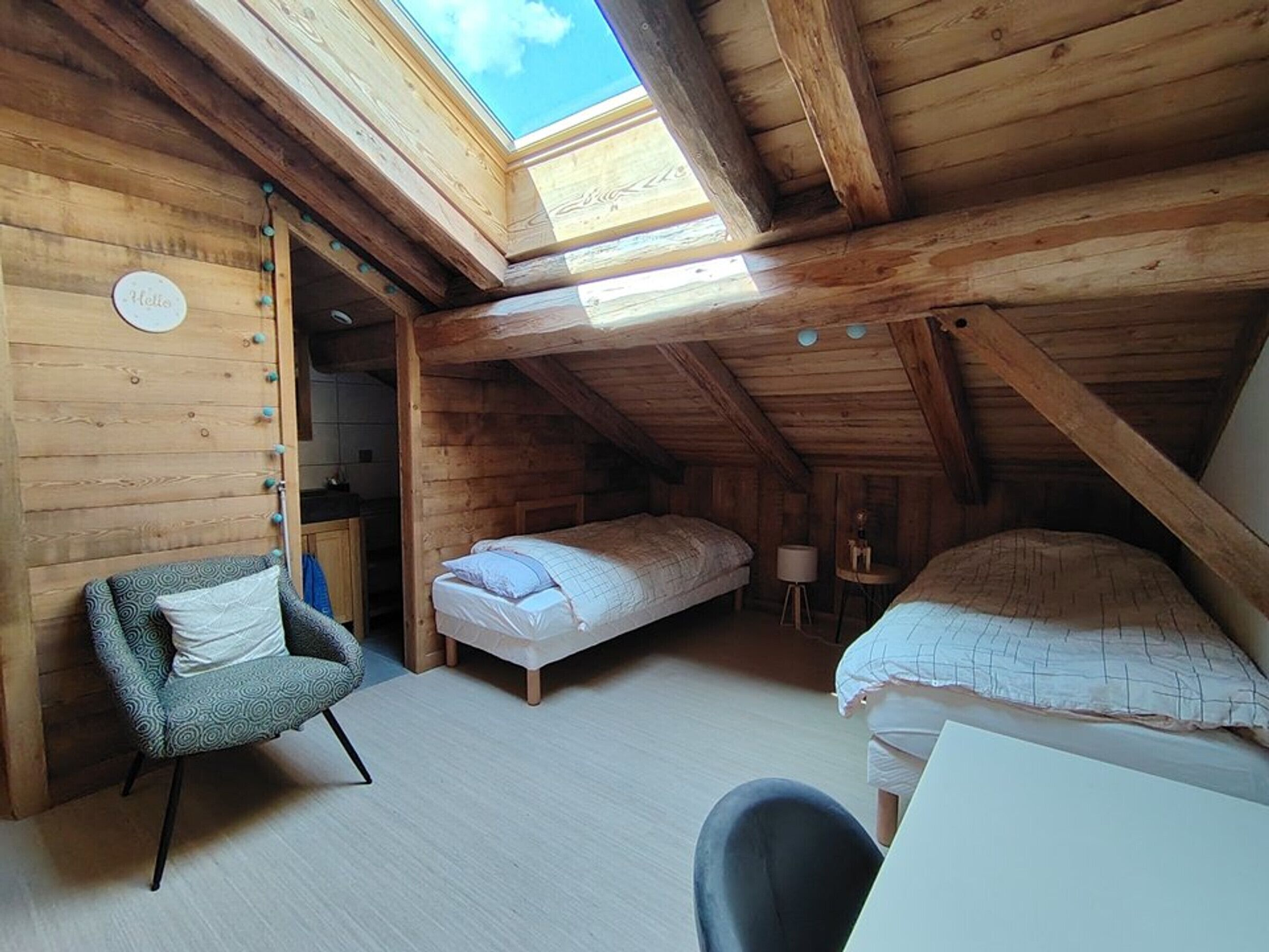 A cozy attic bedroom with a skylight, two beds, a chair, and a desk.