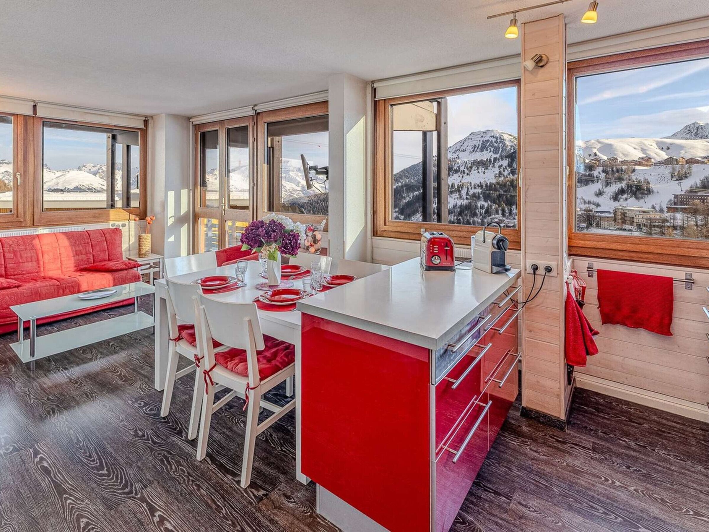 Cocina moderna con una isla central, mesa de comedor y sillas. Amplias ventanas ofrecen vistas a las montañas.