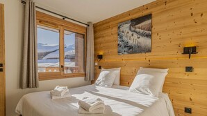 Hotellihuone, jossa on puinen sisustus, valkoisilla lakanoiden peitetty sänky, seinällä taulu ja ikkunasta avautuu näkymä vuorille.