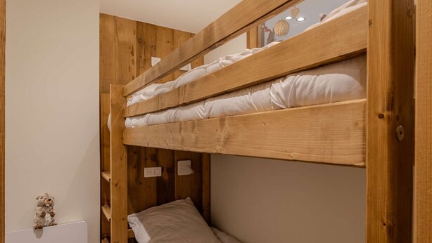 A bunk bed with wooden frames and white bedding.