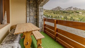 A balcony with a wooden table and bench, stone wall, and a view of mountains.