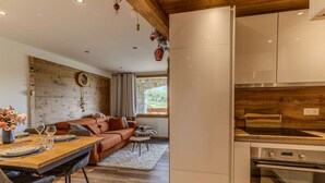 A modern kitchen with stainless steel appliances, a wooden ceiling, and a stone wall.