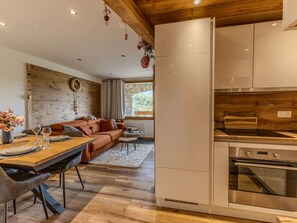 A modern kitchen with stainless steel appliances, a wooden ceiling, and a stone wall.