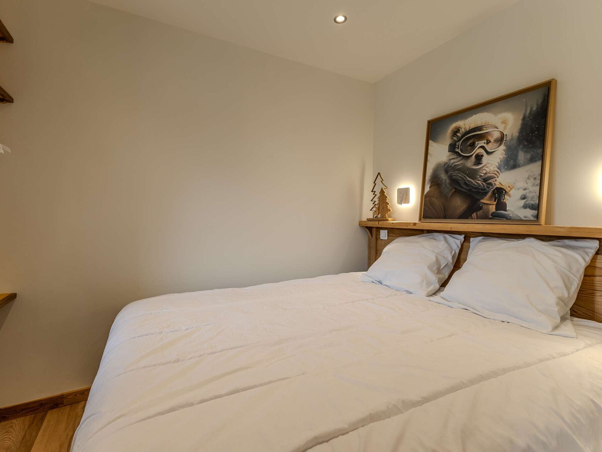 Un dormitorio con una cama grande, cabecera de madera, un cuadro colgado en la pared y una pequeña decoración de árbol de madera.