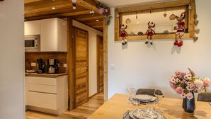 A dining area with a wooden table set for two, a coffee machine, and a microwave in the adjacent kitchen.