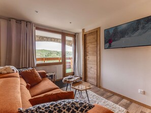 Ett mysigt vardagsrum med en soffa, ett litet bord, en tavla och utsikt över ett snötäckt landskap genom en glasdörr.
