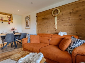 Ein modernes Wohnzimmer mit einer Wand in Holzoptik, einer Couch mit gemusterten Kissen, einem Essbereich mit Stühlen und einer dekorativen Wandgestalt.