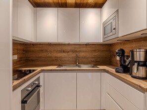 Ett modernt kök med vita skåp, en träpanel bakom arbetsbänken, rostfria vitvaror och en inbyggd mikrovågsugn.