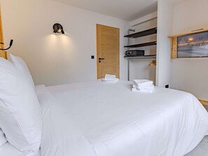 Ein Hotelzimmer mit einem Bett, einer Wandleuchte, einer Holztür, einem Regal mit Handtüchern und einem Bild.