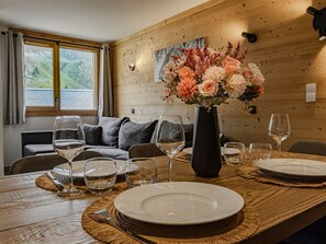 Ein Essbereich mit einem Holztisch, gedeckt für vier Personen, einer Blumenvase und Blick auf eine Berglandschaft durch ein Fenster.