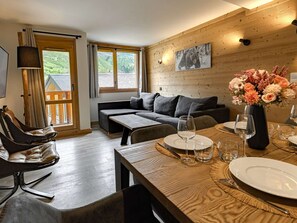 A cozy living room with a sofa, a dining table set for two, and a view of the outdoors through large windows. - Luxury apartment in ski resort center - 6 guests (Belle Plagne)