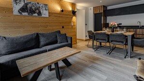 Ein modernes Wohnzimmer mit Sofa, Couchtisch, Essbereich mit Stühlen und einer Küche im Hintergrund.