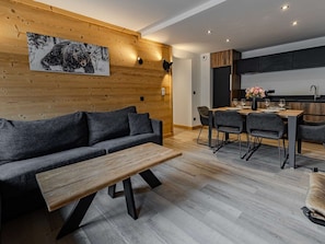 A modern living room with a sofa, coffee table, dining area with chairs, and a kitchen in the background. - Luxury apartment in ski resort center - 6 guests (Belle Plagne)