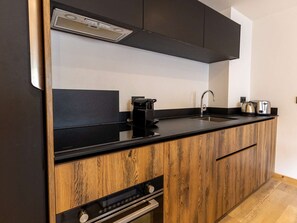 A modern kitchen with a black countertop, wooden cabinetry, a built-in oven, a coffee maker, and a toaster. - Luxury apartment in ski resort center - 6 guests (Belle Plagne)