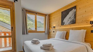 Ein Schlafzimmer mit einem großen Bett, einem hölzernen Kopfteil, einem Gemälde und Blick auf eine Berglandschaft durch ein Fenster.