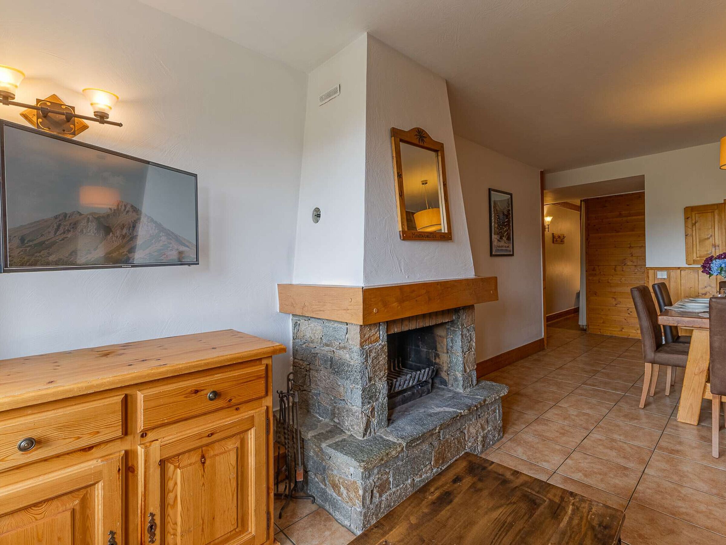 Una habitación con chimenea de piedra, muebles de madera, una mesa de comedor con sillas, un cuadro colgado y un espejo en la pared.