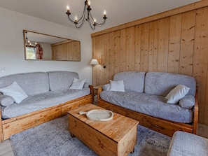 Ein Wohnzimmer mit zwei grauen Sofas, einem Holztisch, einer Deckenleuchte und einer Holzwandverkleidung.