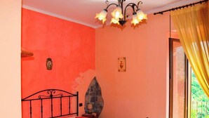 A room with a bed, a stone fireplace, a chandelier, and a window with yellow curtains.
