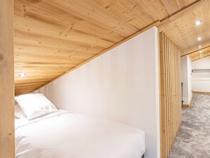 Een slaapkamer met schuin dak, een bed met wit beddengoed en een houten scheiding.