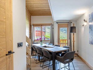 Ein Essbereich mit einem Holztisch und Stühlen, einer Vase mit Blumen und Blick auf eine Berglandschaft durch die Fenster.