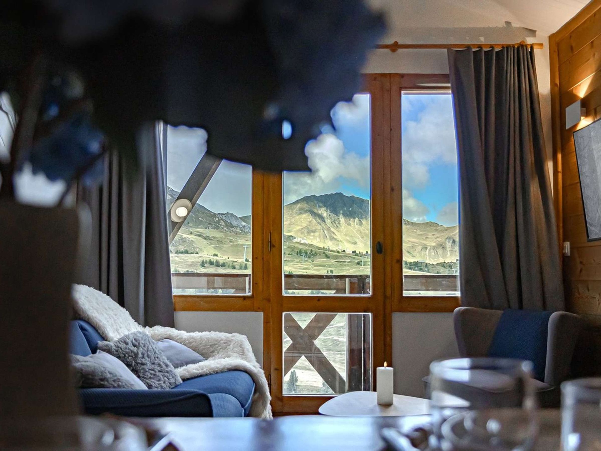 Ein Zimmer mit einem Bett, einem Tisch mit Kerze und großen Fenstern mit Bergblick.