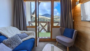 Una habitación con sofá, una silla, una mesa y vistas a montañas a través de amplios ventanales.