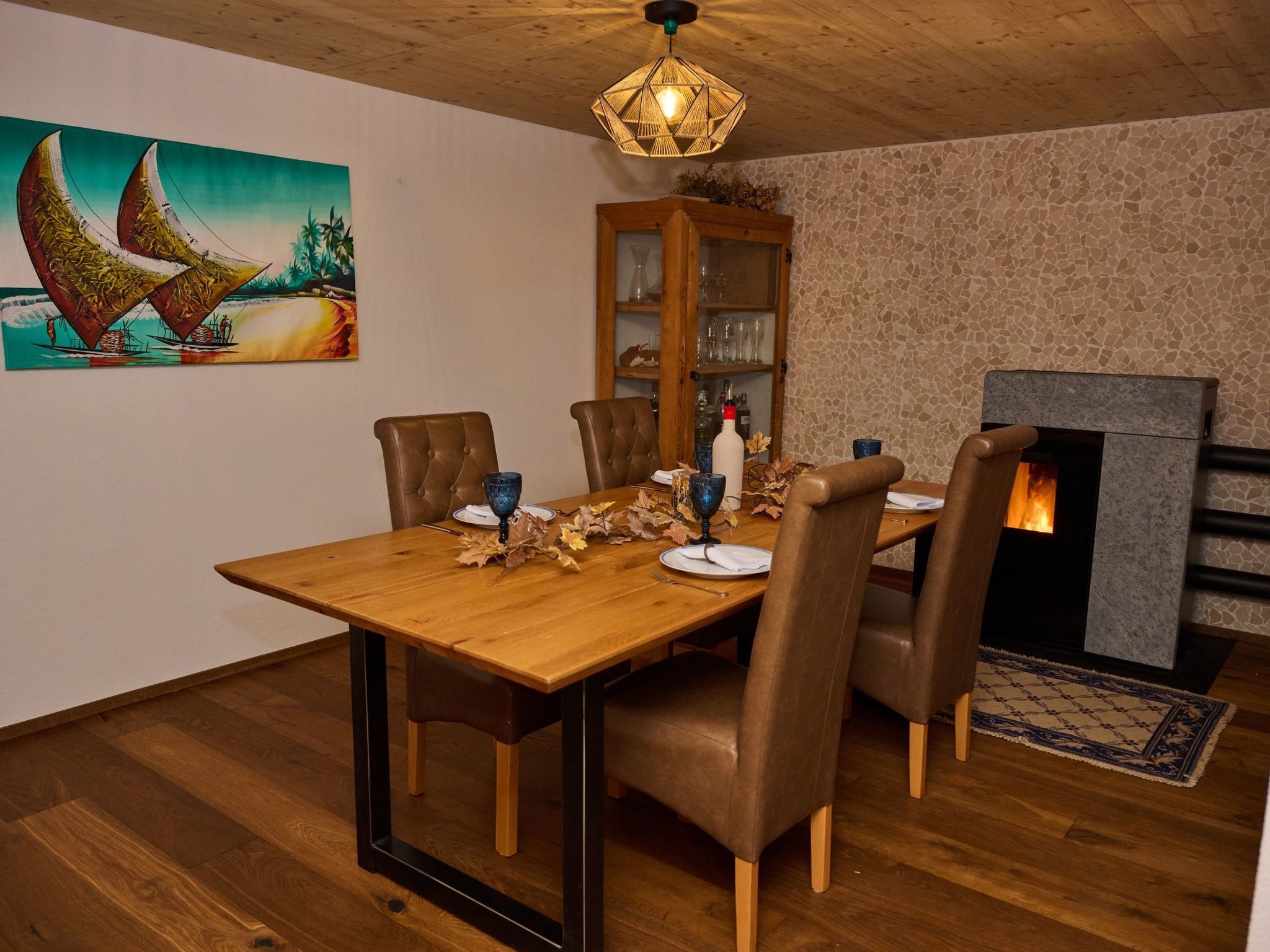 Une salle à manger avec une table en bois, des chaises à revêtement marron, une vitrine et une cheminée.