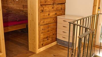 A wooden interior with a bed, a dresser, and a staircase.