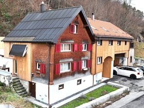 Ein zweistöckiges Haus mit geneigtem Dach, roten Fensterläden und einer Solaranlage auf dem Dach.