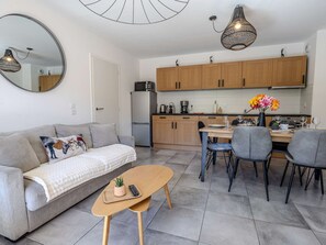 Ein kompakter Wohnbereich mit einer Couch, einem Couchtisch, einer Essecke mit Stühlen, einer Küche mit Holzschränken und einer Pendelleuchte.