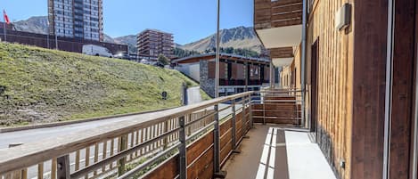 A wooden balcony with a metal railing overlooking a hillside and buildings.