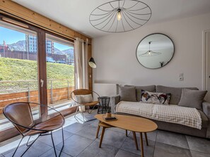 Ein modernes Wohnzimmer mit einer Couch, einem Couchtisch und einem Sessel. Es gibt ein großes Fenster mit Blick auf einen Berg und ein Gebäude.