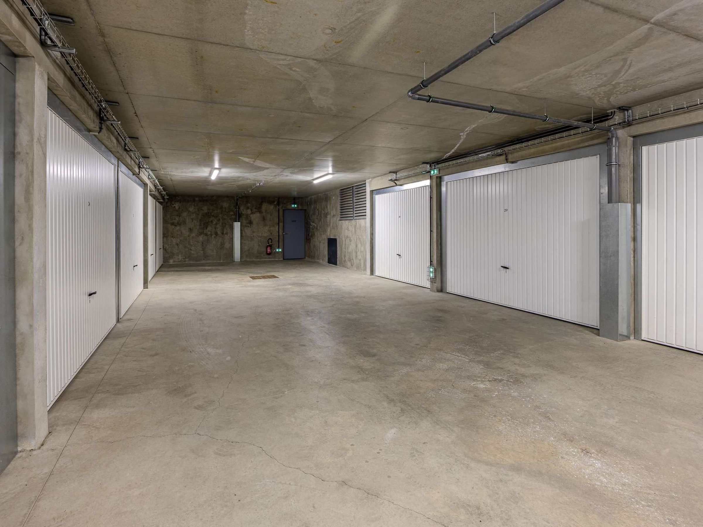A clean, empty hallway with white doors and a concrete floor, leading to a door at the end.