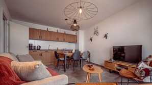 Uma sala de estar moderna com sofá, mesa de centro, TV e área de jantar com cadeiras e mesa.