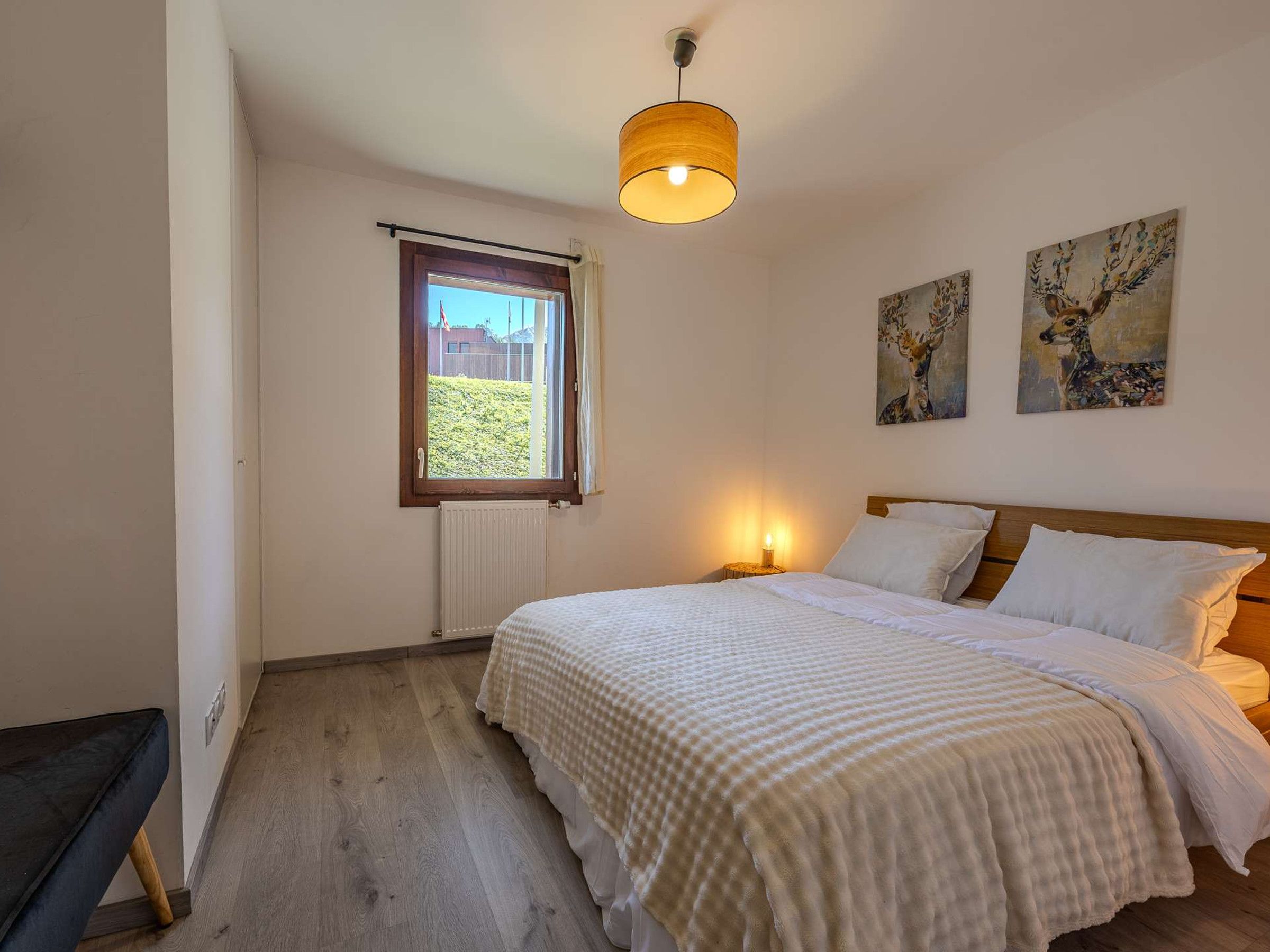Une chambre à coucher avec un lit, une fenêtre, un radiateur et deux tableaux accrochés au mur.