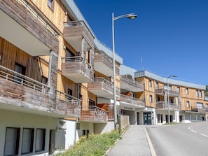 Un immeuble résidentiel moderne à plusieurs étages, doté de balcons, d’un lampadaire et surplombant un ciel bleu dégagé.