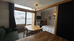 A room with a wooden table and chairs, a bunk bed, a television, and a large window with a view of a snowy landscape. - Modern studio at the foot of the slopes - 6 guests (Plagne Bellecôte)